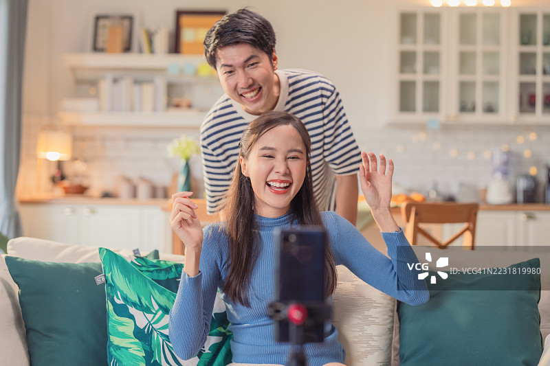 亚洲女性为她的社交平台创作病毒式微内容，拍摄真实的舞蹈和唱歌时刻，男朋友在背景中搞怪入镜。图片素材