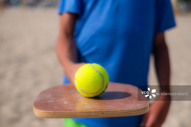 一个青少年在木制球拍上保持一个球的平衡图片素材
