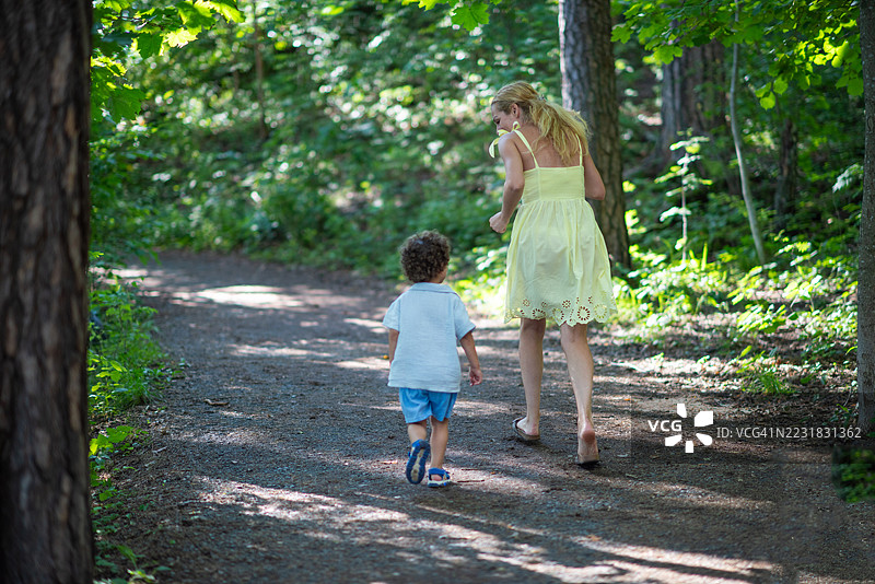 阳光明媚的夏日，女性和小男孩在森林中慢跑的背影。图片素材