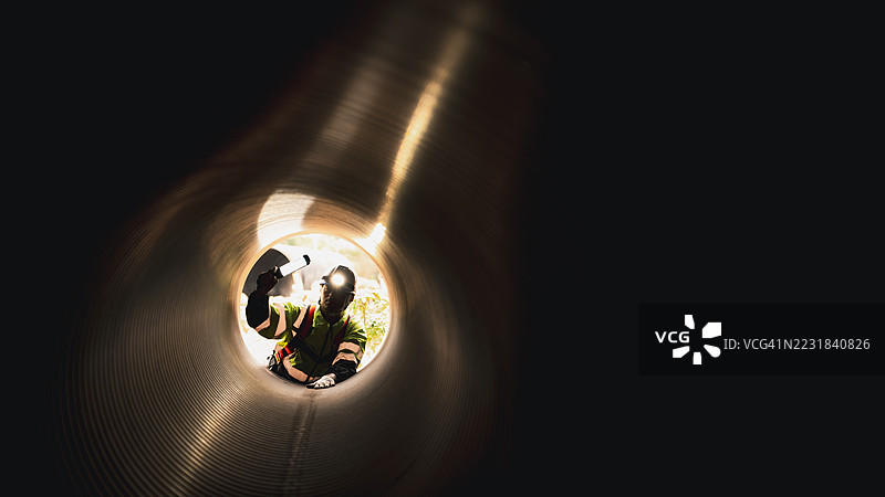 工人在繁忙的工业现场内的巨大钢管道中作业，建设石油、天然气和燃料的基础设施。图片素材