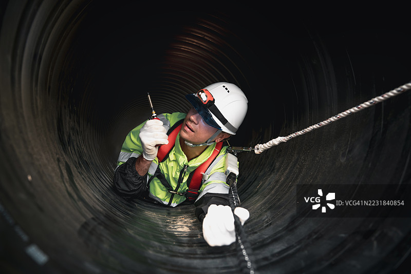 工人在繁忙的工业现场内的巨大钢管道中作业，建设石油、天然气和燃料的基础设施。图片素材