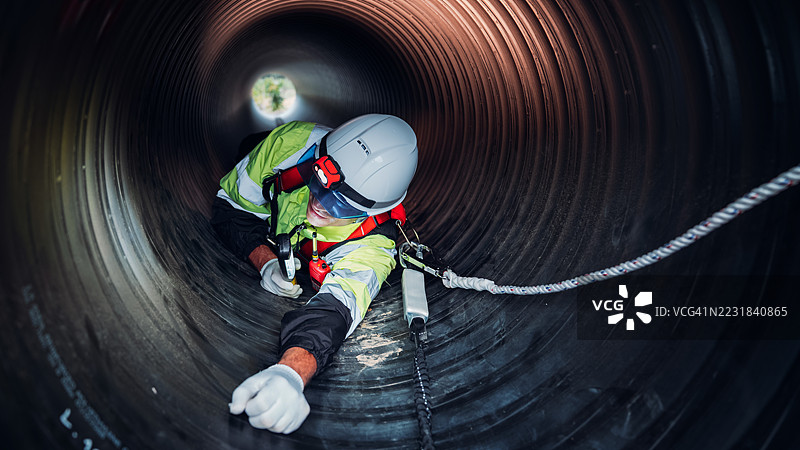 工人在繁忙的工业现场内的巨大钢管道中作业，建设石油、天然气和燃料的基础设施。图片素材