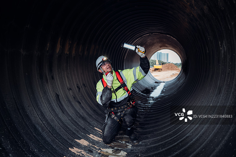 工人在繁忙的工业现场内的巨大钢管道中作业，建设石油、天然气和燃料的基础设施。图片素材