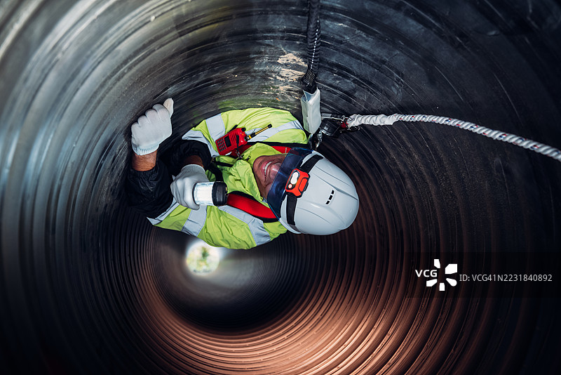 工人在繁忙的工业现场内的巨大钢管道中作业，建设石油、天然气和燃料的基础设施。图片素材