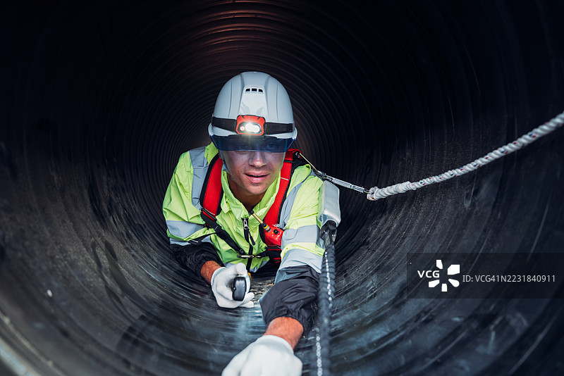 工人在繁忙的工业现场内的巨大钢管道中作业，建设石油、天然气和燃料的基础设施。图片素材