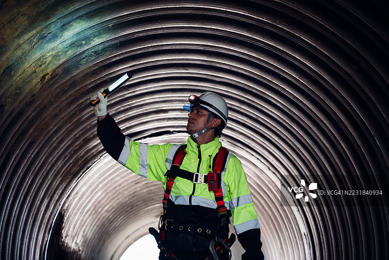 工人在繁忙的工业现场内的巨大钢管道中作业，建设石油、天然气和燃料的基础设施。图片素材