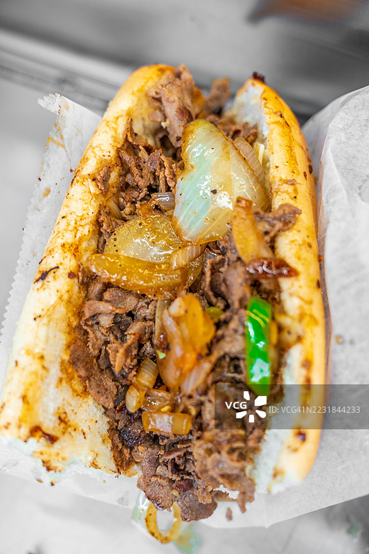 在街头节日上供应的洋葱和辣椒满载的费城奶酪牛排三明治。图片素材