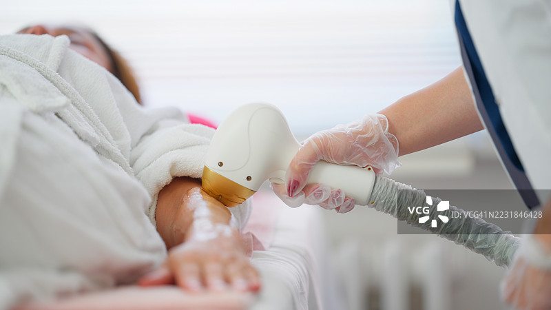 美容师使用激光脱毛仪去除女性手臂上的汗毛图片素材