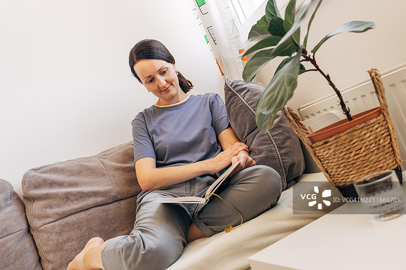 女人在舒适的客厅沙发上放松，阅读一本书图片素材
