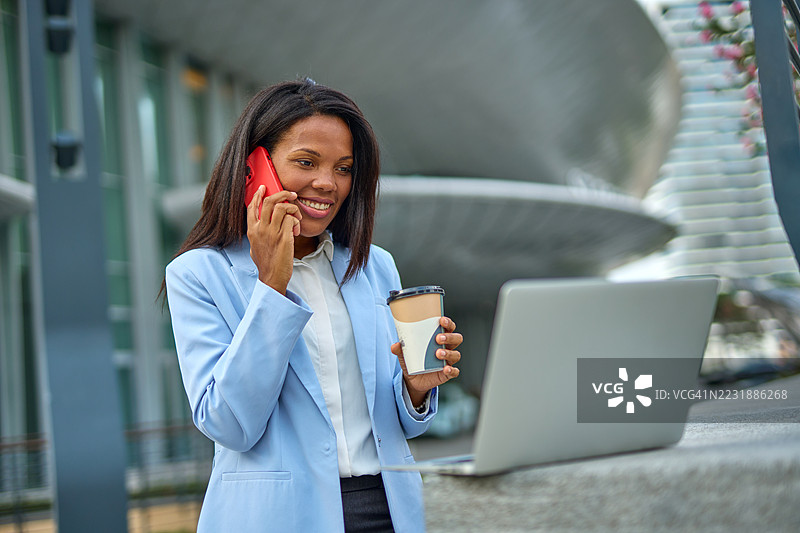 商务女性在户外一边喝咖啡一边打电话和使用笔记本电脑图片素材