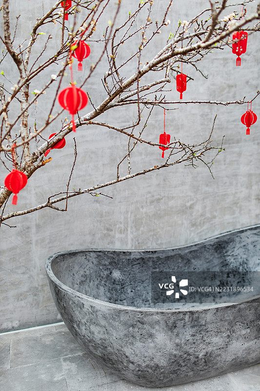 现代石浴缸与装饰树相映衬，背景为灰色墙壁。奢华浴室。图片素材