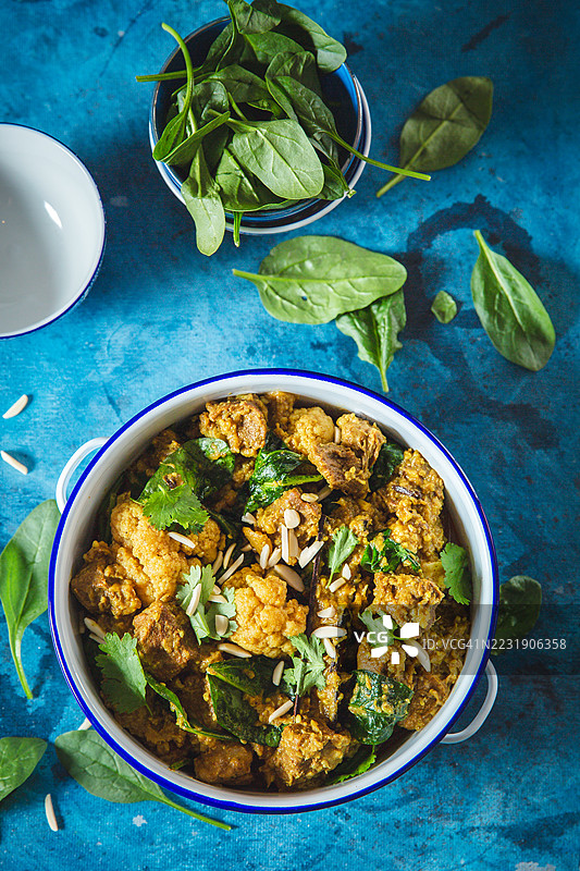美味的香料牛肉咖喱配菠菜和杏仁，背景为装饰性的蓝色图片素材