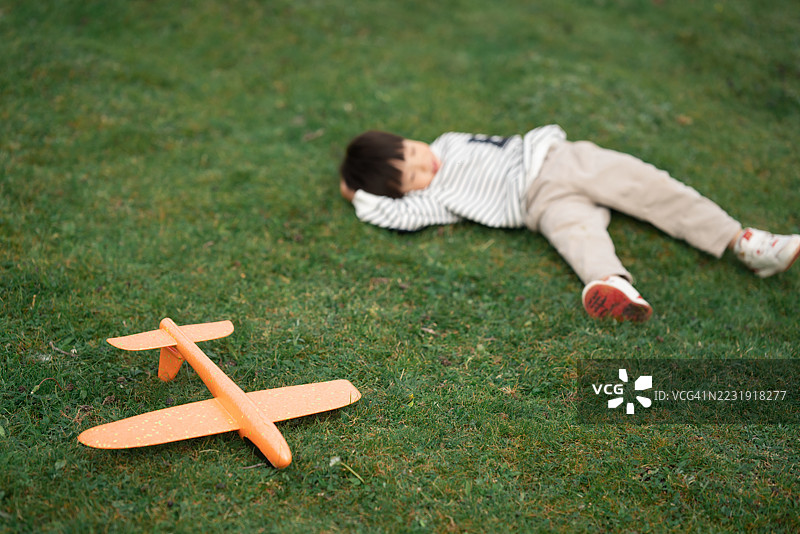 亚洲三岁小孩在草地上玩飞机模型图片素材