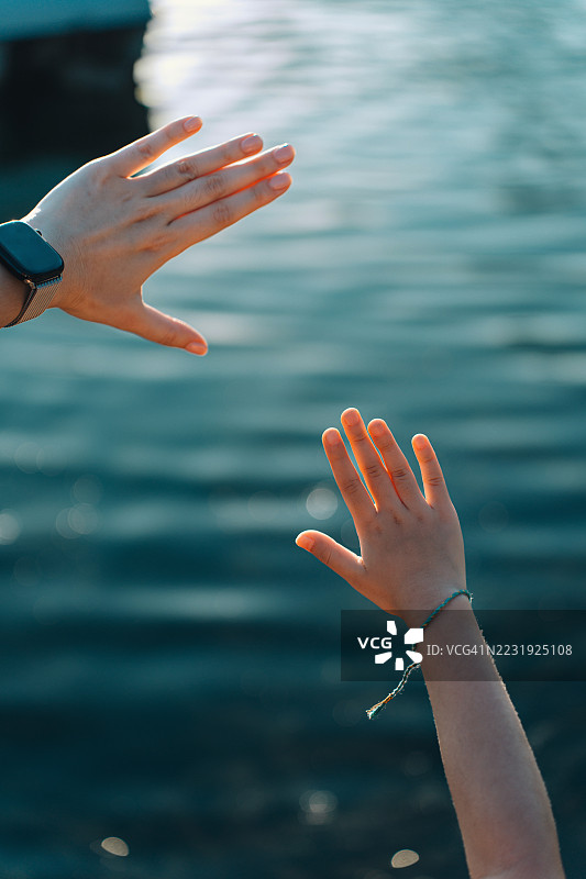 亚洲母女在公园的池塘边，夕阳下抬起手迎接阳光，仰望美丽的风景。她们在享受新鲜空气的同时，放松心情，珍惜母女时光。家庭生活，爱与团聚。图片素材