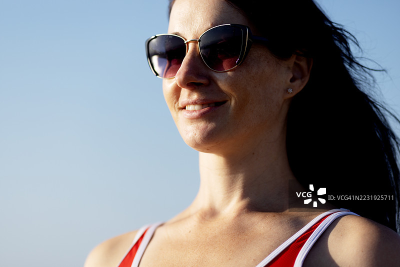 微笑的女性在阳光明媚的海滩上晒太阳。健康生活和自我护理的概念。防止紫外线辐射的眼部保护。图片素材