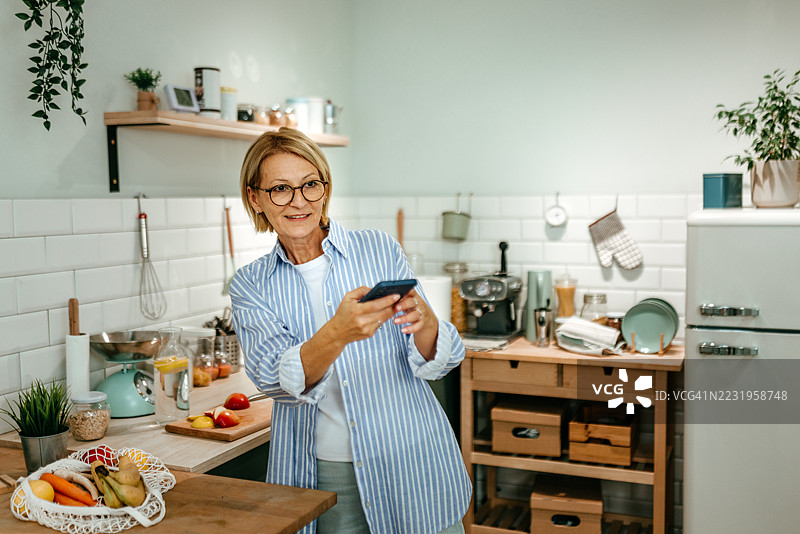 女性使用智能手机控制厨房中的智能设备图片素材