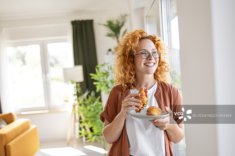 女人在窗边品味新鲜可颂三明治的香气图片素材