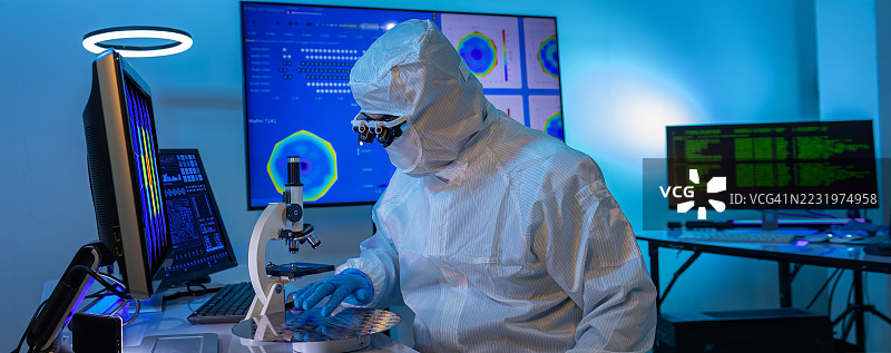 电子制造厂的半导体生产。工人或工程师穿着医疗防护服或白色工作服，手持硅晶圆。图片素材