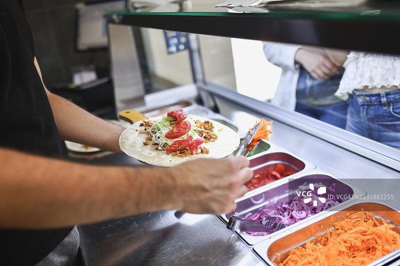 男性在顾客等待时为玉米饼添加色彩丰富的蔬菜图片素材