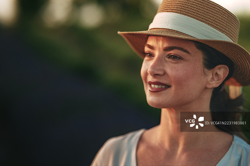 戴着草帽的女人在日落时分的薰衣草田里微笑图片素材