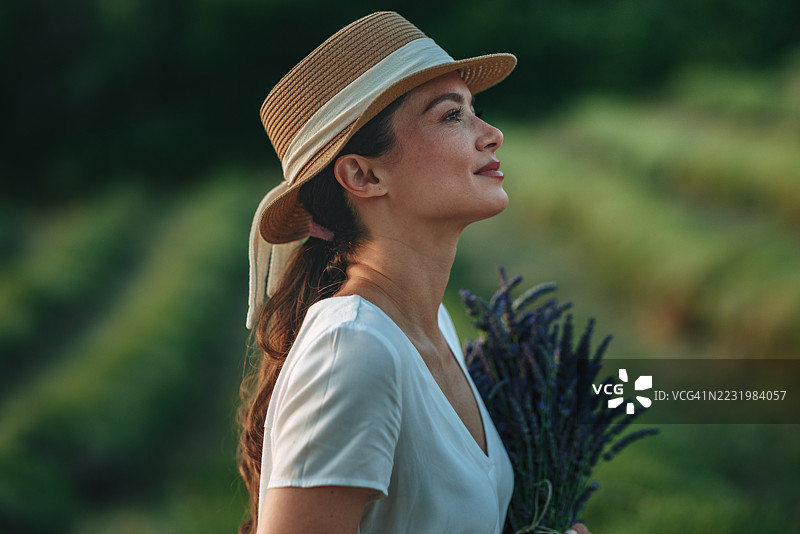 戴着草帽的女人在田野中手持薰衣草花束图片素材