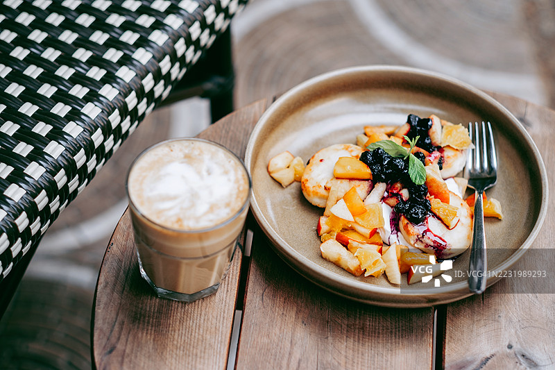 一盘农家奶酪煎饼或里可塔芝士蛋糕，上面饰有浆果、桃子片和糖浆，旁边放着一杯拿铁。早餐、甜点和咖啡休息的概念。图片素材