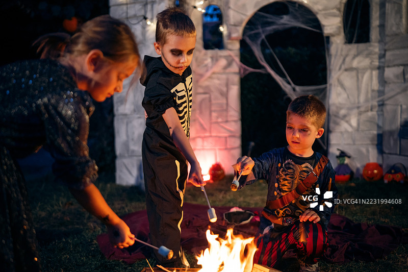 孩子们在万圣节夜晚的后院篝火旁聚会，烤棉花糖，享受美好时光。图片素材