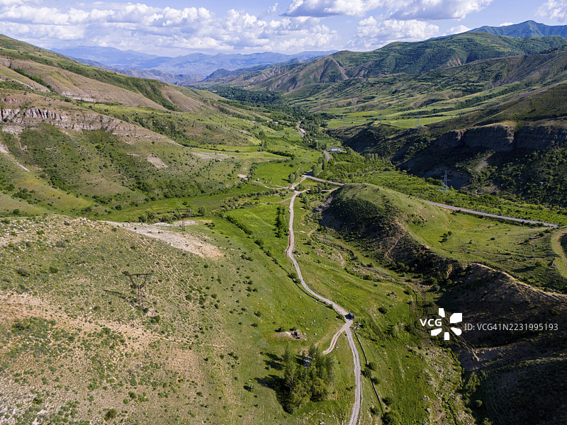 一条蜿蜒的小路穿过绿色的山谷，旁边有一条小溪和环绕的山丘，鸟瞰图，位于阿赫贾扎尔附近，瓦尔德尼斯山脉，瓦约茨·佐尔省，丝绸之路，亚美尼亚图片素材