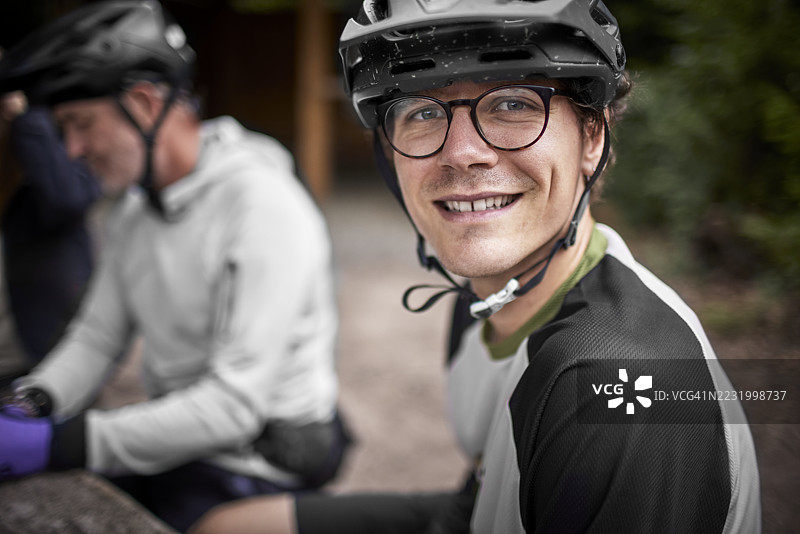 森林里，一位面带微笑的山地自行车手正与朋友们一同休息，拍摄肖像照。图片素材