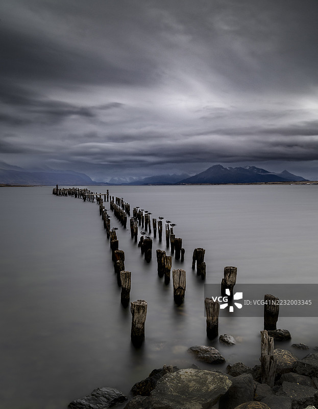 智利平静海面上方的戏剧性多云天空与风化的木桩图片素材