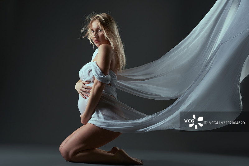 孕妇身披飘逸的织物，置身于深色背景前图片素材
