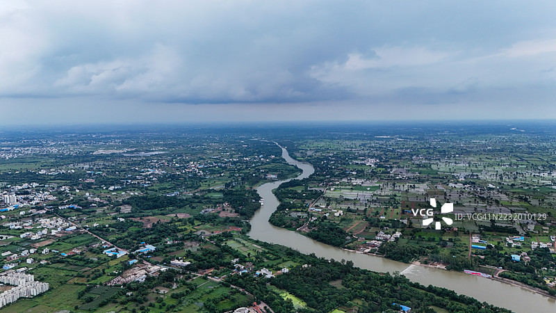 城市和农田下，河流蜿蜒而过的鸟瞰图，天空多云。图片素材