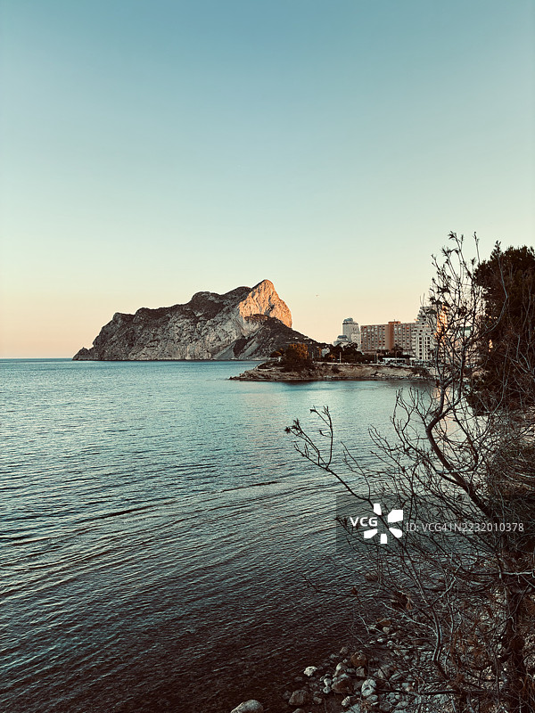 日落时分的海岸风景，背景是山脉和建筑，西班牙卡尔普图片素材
