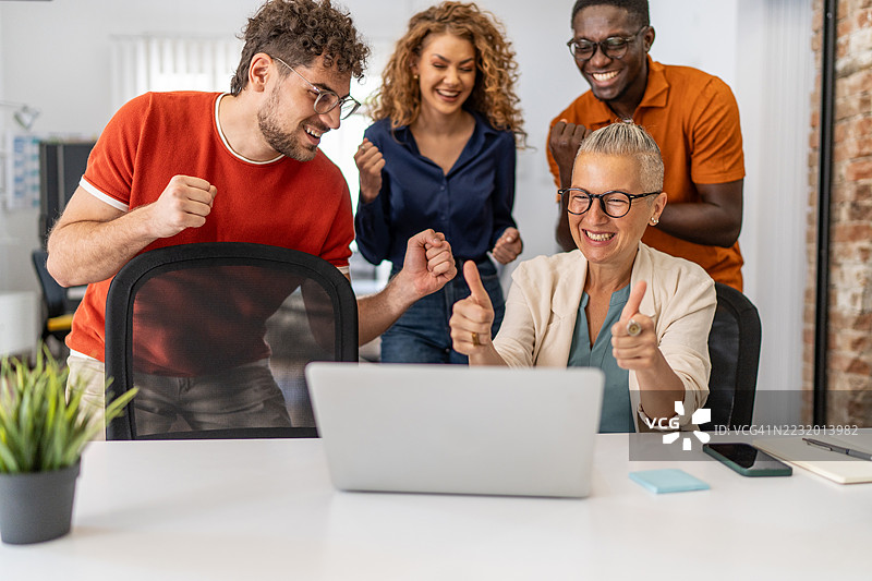 兴奋的商务团队在办公室庆祝成功，使用笔记本电脑。图片素材