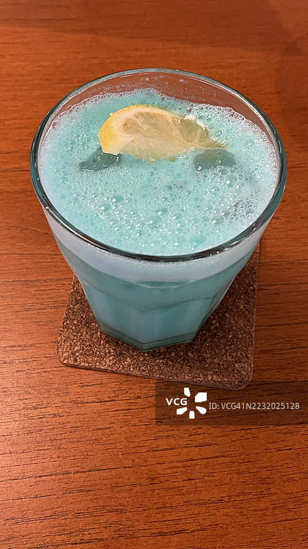 高角度视图的蓝色鸡尾酒，配有柠檬片，放在木桌上图片素材