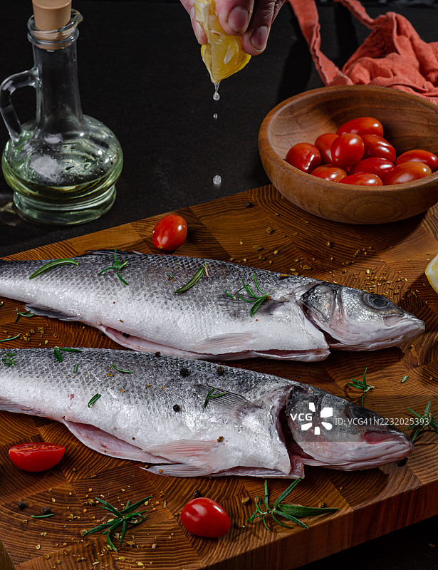 新鲜鱼配柠檬和樱桃番茄放在木板上图片素材