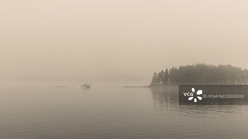 芬兰约乌岑诺的雾气弥漫的湖泊，湖中有船和森林小岛图片素材