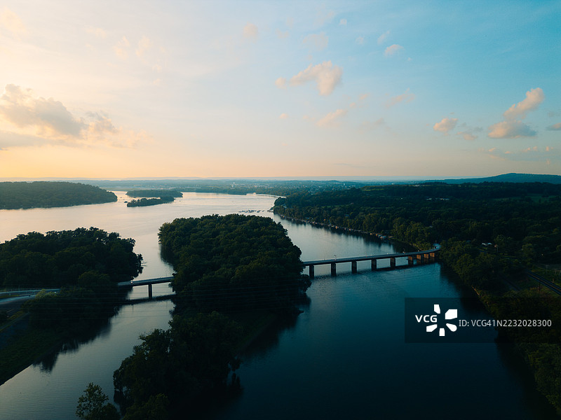 日落时分，郁郁葱葱的绿树环绕下的河流和桥梁的鸟瞰图图片素材