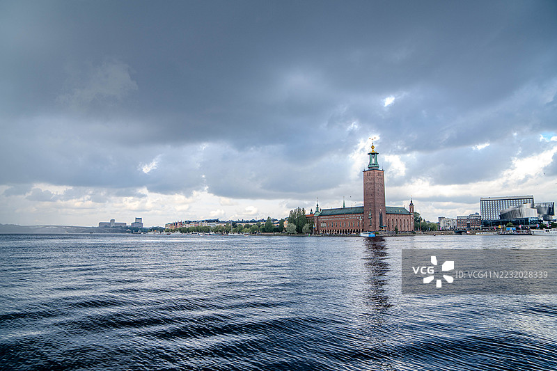 斯德哥尔摩市政厅位于水边，云层密布的天空下，瑞典斯德哥尔摩图片素材