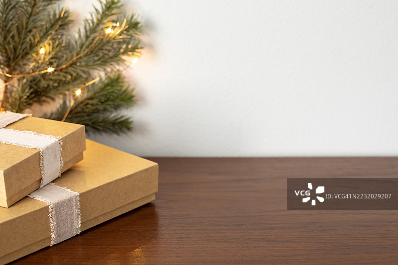 木桌上摆放着圣诞礼物，旁边有松枝和灯光。图片素材