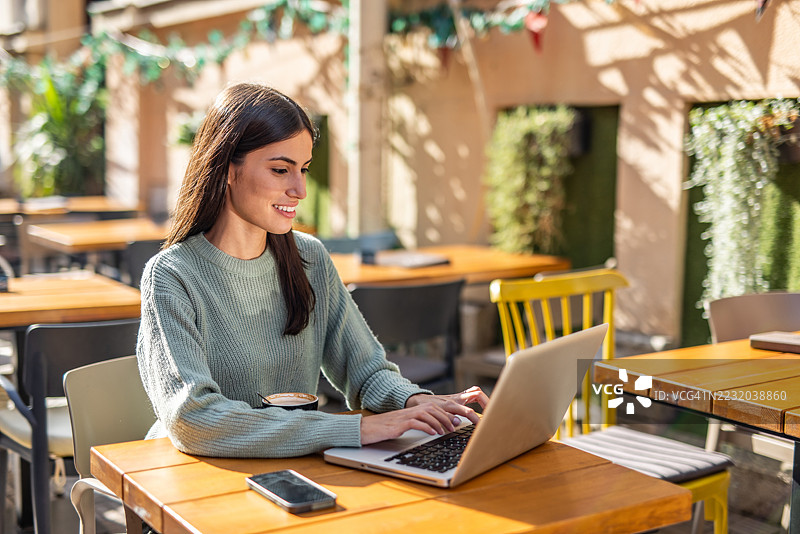 年轻女性在户外咖啡馆使用笔记本电脑工作图片素材