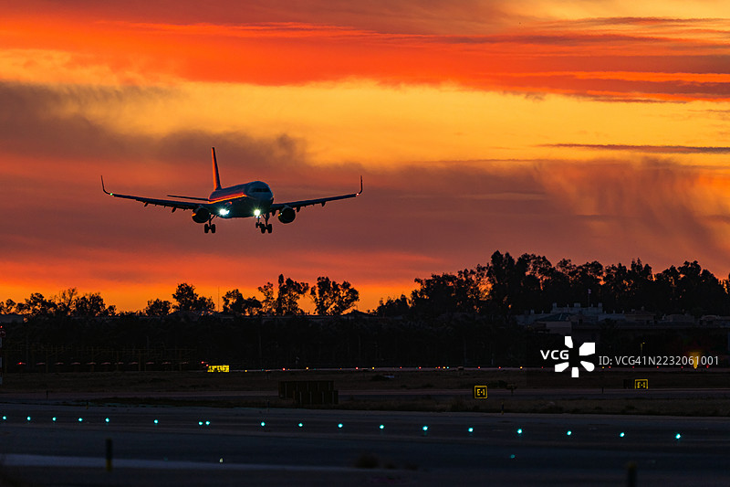飞机在日出时分降落在灯光照亮的跑道上。图片素材