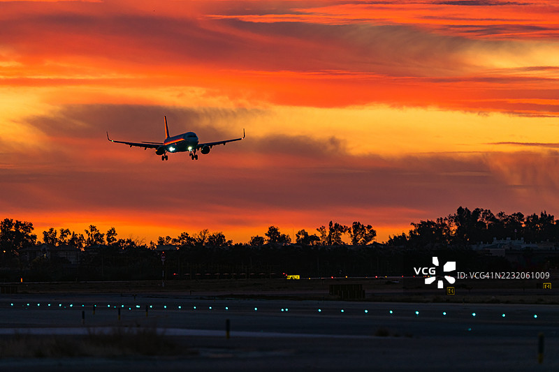 飞机在日出时分降落在灯光照明的跑道上。图片素材