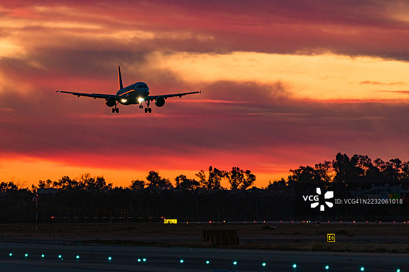 飞机在日出时分的跑道上降落，跑道灯光闪烁。图片素材