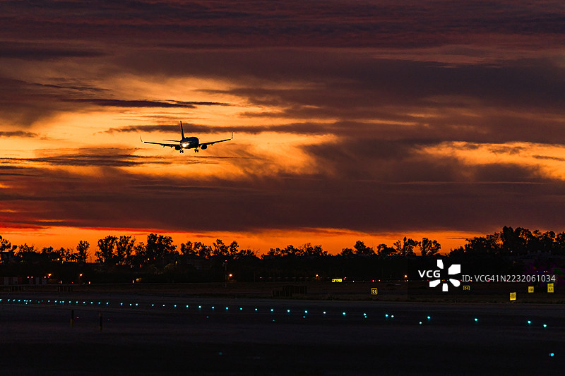 飞机在日出时分的跑道上降落，跑道灯光闪烁。图片素材