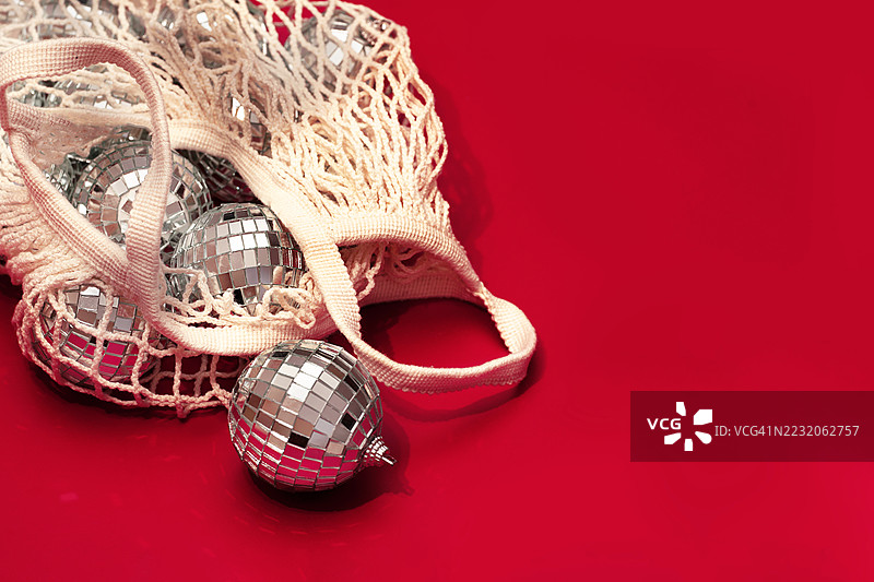 当代艺术概念。银色迪斯科球放在红色背景的网购物袋上。圣诞快乐和新年快乐的邀请。图片素材