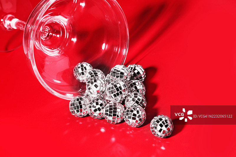 当代艺术拼贴。概念是银色迪斯科球从鸡尾酒杯中滚出，背景为红色。圣诞快乐和新年快乐的邀请。图片素材