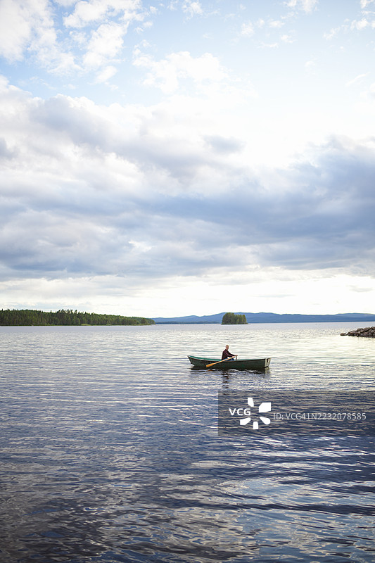年轻男子在日落时划船于湖上图片素材
