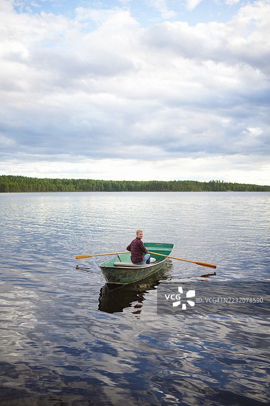 年轻男子在日落时划船于湖上图片素材