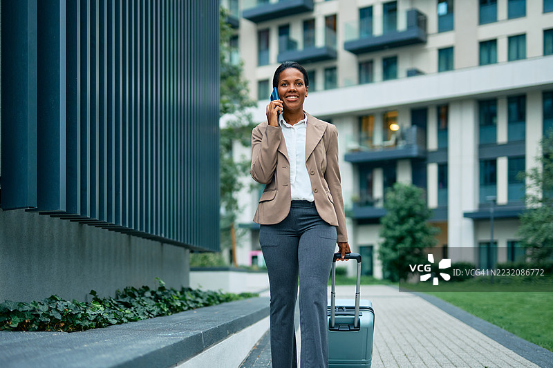 商务女性一边走一边拖着行李箱，边打电话。图片素材
